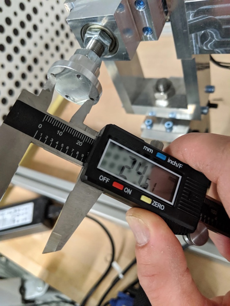 A digital caliper measuring a machined aluminium part on a test rig