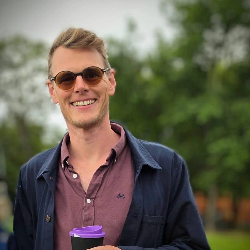 Trygve smiling outdoors in round sunglasses, holding a coffee cup